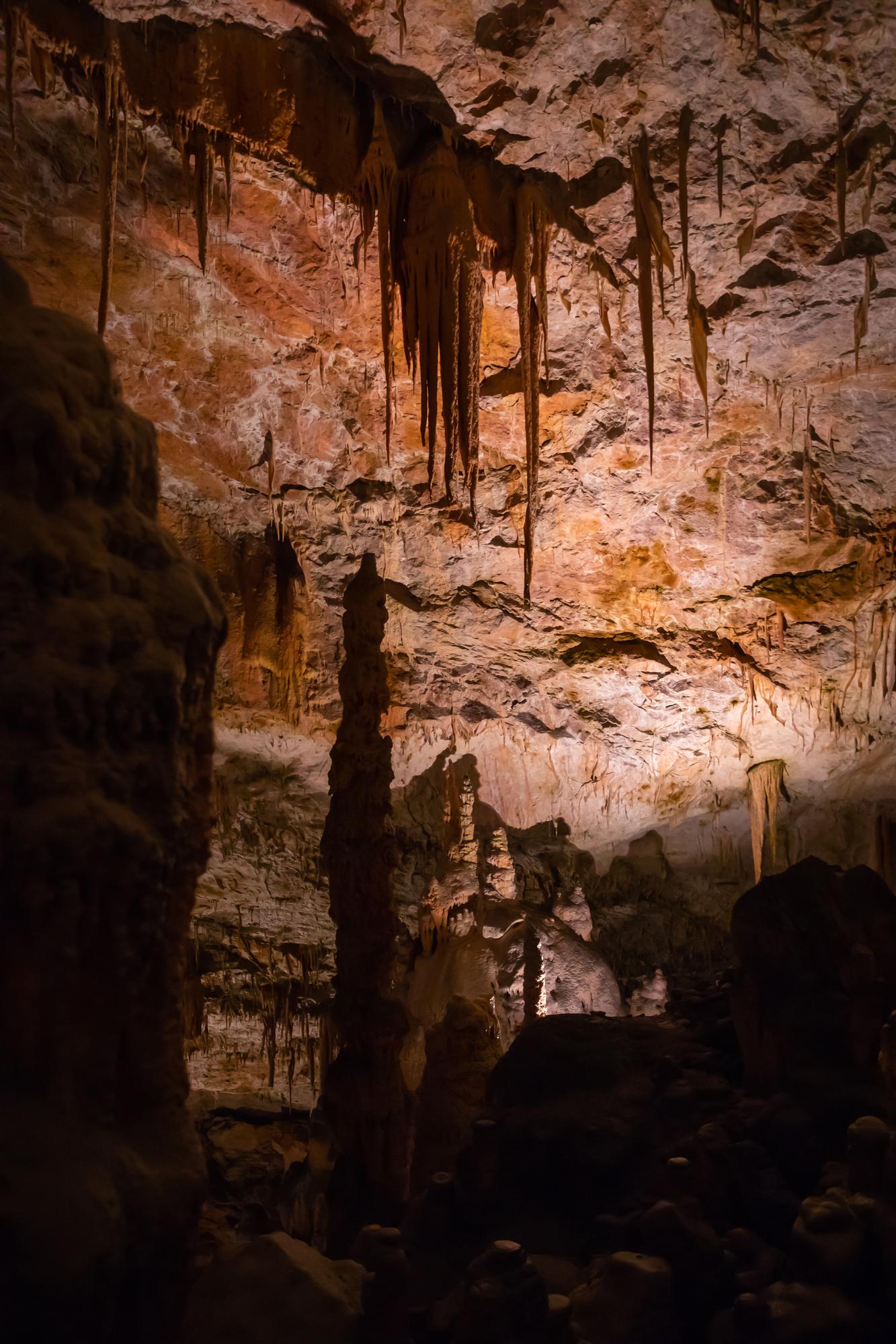 Estalactites e coluna de estalagmite em caverna calcária iluminada.